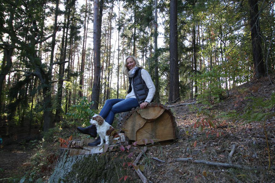 Maike Tielking im Wald, auf einem Baumstumpf sitzend, mit ihrem Hund